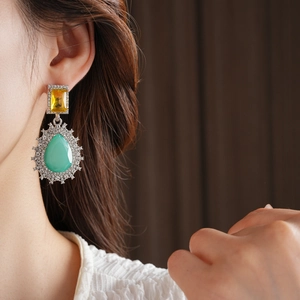 Gros plan de boucles d'oreilles vintage avec gemmes jaunes et pendentifs goutte verts