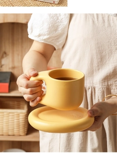 Yellow ceramic chubby coffee mug and saucer set held by hands in a warm home setting