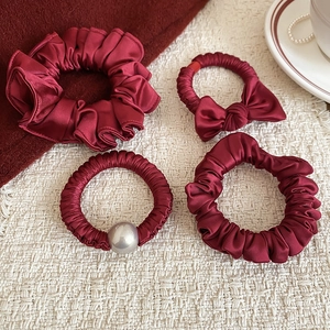 Detailed set of burgundy satin scrunchies and bow with large pearl accent on tray