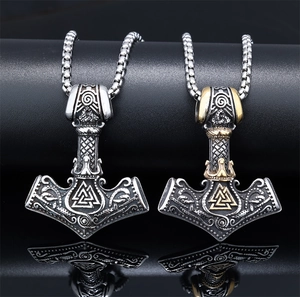 Macro detail of Viking Mjolnir pendants in silver and gold tone on a reflective surface