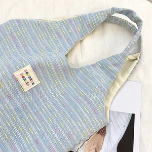 Close-up of sky blue tweed tote bag showing woven texture and embroidered label detail