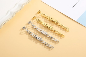 Close-up of gold and silver long chain earrings with LOVE letter pendants on a beige base