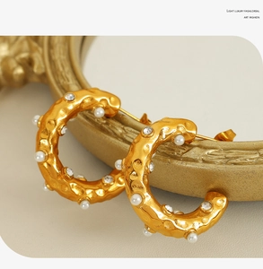 Detail of C-shaped 18K gold plated earrings with hammered texture and pearl inlay