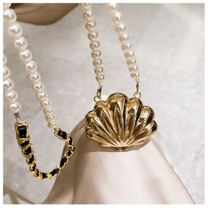 Detailed macro view of golden shell mini bag with pearl chain and woven leather strap