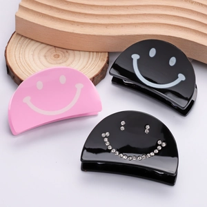 Three acrylic smiley face hair claws in pink, black, and rhinestone-studded styles