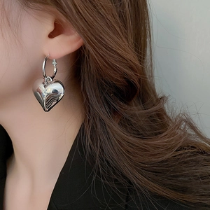 Close-up of polished silver heart-shaped dangle earrings on a model in a black suit