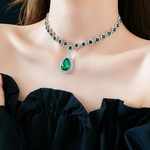 Primo piano di una collana con una grande gemma verde a goccia sul collo di un modello