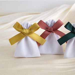 Three white velvet jewelry pouches featuring elegant gold, pink and dark green silk bows