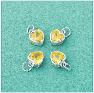 Macro shot of S925 sterling silver heart pendants with yellow zircon inlays on green texture