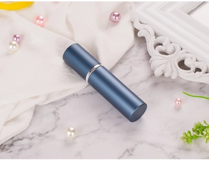 Detail view of a matte blue aluminum spray bottle on a white marble background with pearls