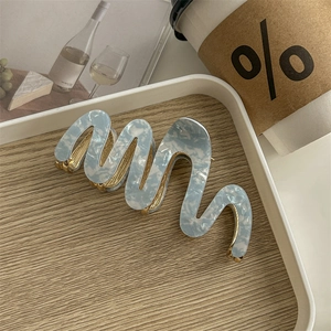 Detail of light blue acetate hair claw clip with gold trim on a minimalist wooden tray