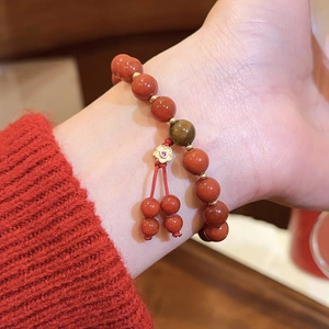 Nahaufnahme eines roten Achat-Perlenarmbands mit goldenem Blumenanhänger und Tigerauge-Perle
