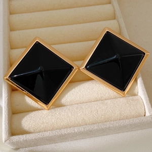 Macro shot of gold-plated square studs with black enamel in a beige velvet jewelry box