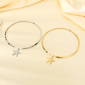 Detail of silver and gold starfish pendants on rigid necklaces over beige silk fabric