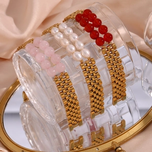 Detailed shot of gold watch-band style bracelets with natural stones and pearls on a mirror