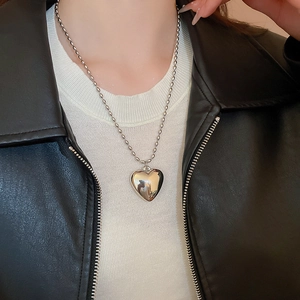 Close-up of a polished gold heart pendant with a bead chain worn on a leather jacket