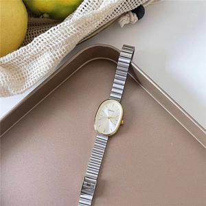 Macro view of oval gold case quartz watch and silver metal band on champagne tray