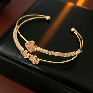 Close-up of rose gold four-leaf clover bracelet with pink zircons on black leather