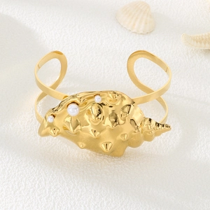 Macro shot of gold-plated seashell bracelet with pearl accent on sandy texture