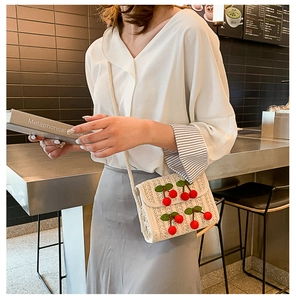 Straw bag with 3D cherry accents worn by a model in a cozy cafe setting for summer fashion
