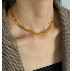 Close-up of a wide gold woven mesh choker necklace worn with a stylish brown checkered blazer