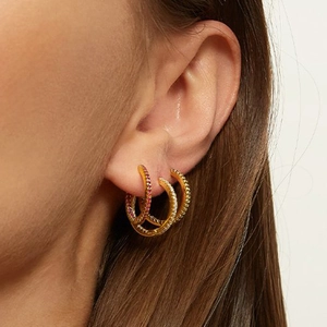 Three-piece set of gold hoop earrings with red and white zircons worn on model ear
