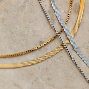 Close-up of gold and silver layered snake and box chains on a textured marble background