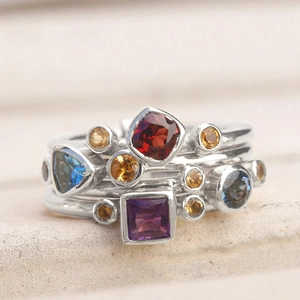 Primer plano de anillos apilables con gemas geométricas de colores y acabado plateado