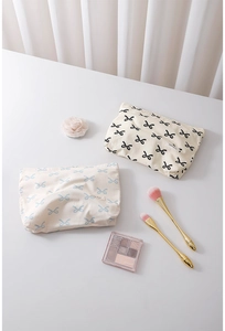 Detailed view of canvas cosmetic bags with bow prints and zip closure on white desk