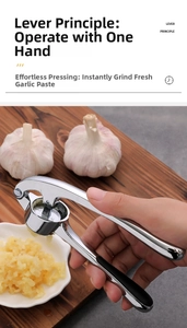 Manual garlic press in action over a dark wooden board showing lever extrusion detail