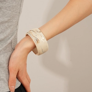 Close-up of a wide marble pattern resin bangle in cream beige worn by a model