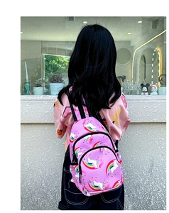 Vista trasera de una niña con mochila de unicornio rosa y morada y estampados de arcoíris