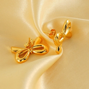 Close-up of golden bow-shaped stud earrings on elegant silk background with 18K finish