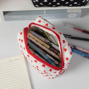 Detail of white quilted cotton pouch with red hearts holding colorful pens on a desk