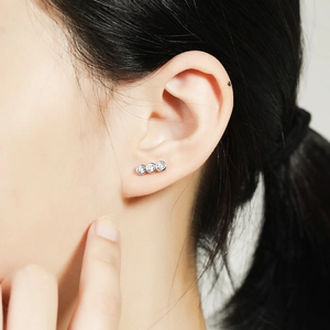 Close-up of minimalist silver stud earrings with three round cubic zirconia on a model