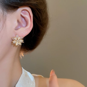 Close-up of golden flower stud earrings with cat eye stone and zircon on a model