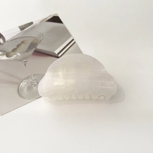 Elegant pearly white half-moon hair claw clip with fine glitter on a stylish white desk