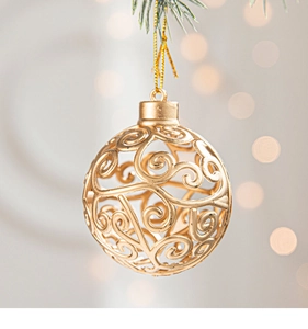 Detail of a golden hollow Christmas ball with vine patterns hanging on a green pine tree