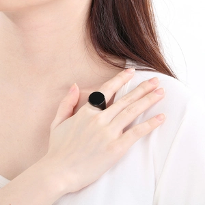 Close-up of a minimalist black circular signet ring on a finger with a polished finish