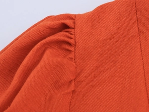 Detail view of orange cotton linen dress shoulder with elegant pleated stitching textures
