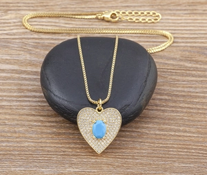 Detailed close-up of a gold heart pendant featuring a blue oval gemstone on a smooth stone