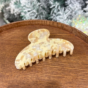 Large marbled acetate claw clip in cream and beige on a wooden display with holiday decor
