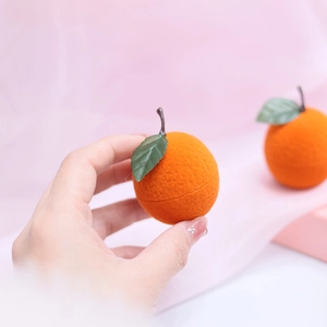 Cute orange fruit shaped jewelry box with green leaf detail held in hand on pink fabric