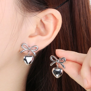 Close-up of a silver bow and heart earring worn on ear with polished metal finish