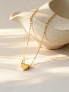 Polished 18k gold heart pendant necklace hanging on a ceramic dish with shadows