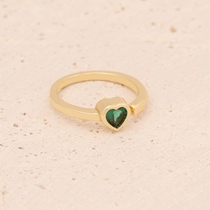 Close-up of golden ring featuring a heart-shaped green gemstone on beige stone surface