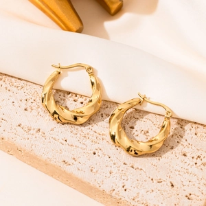 Detailed close-up of golden twisted hoop earrings on elegant silk and stone surface