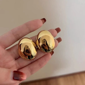 Minimalist oval pebble-shaped gold earrings with high-polished mirror finish in hand