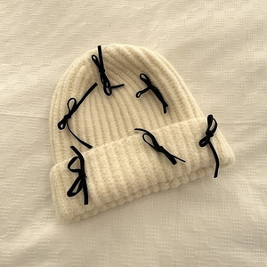Winter beige knit beanie with black velvet bows decoration in a flat lay minimalist view