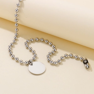 Collier chaîne à billes argentée avec pendentif rond minimaliste sur fond beige neutre